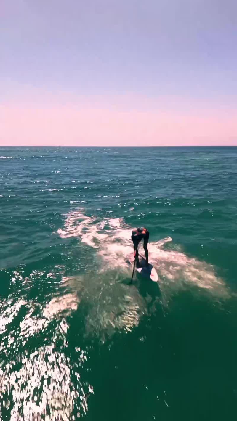 Vertical aerial follow of a foiler riding a wave in clear green water