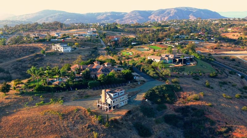 Aerial approach over a hillside estate with the valley and mountains behind it