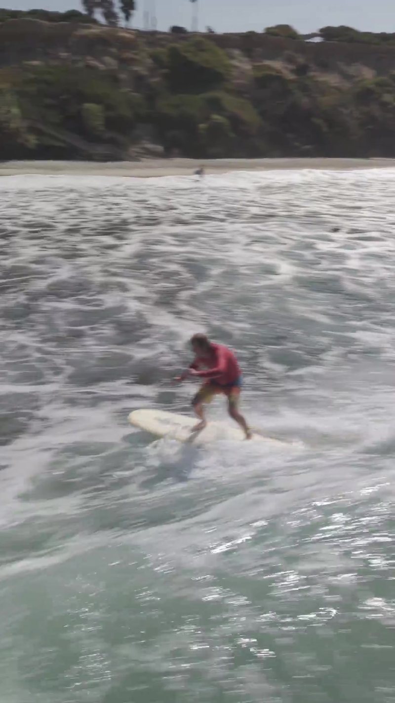 Vertical aerial follow of a surfer riding a wave in toward the beach at Encinitas