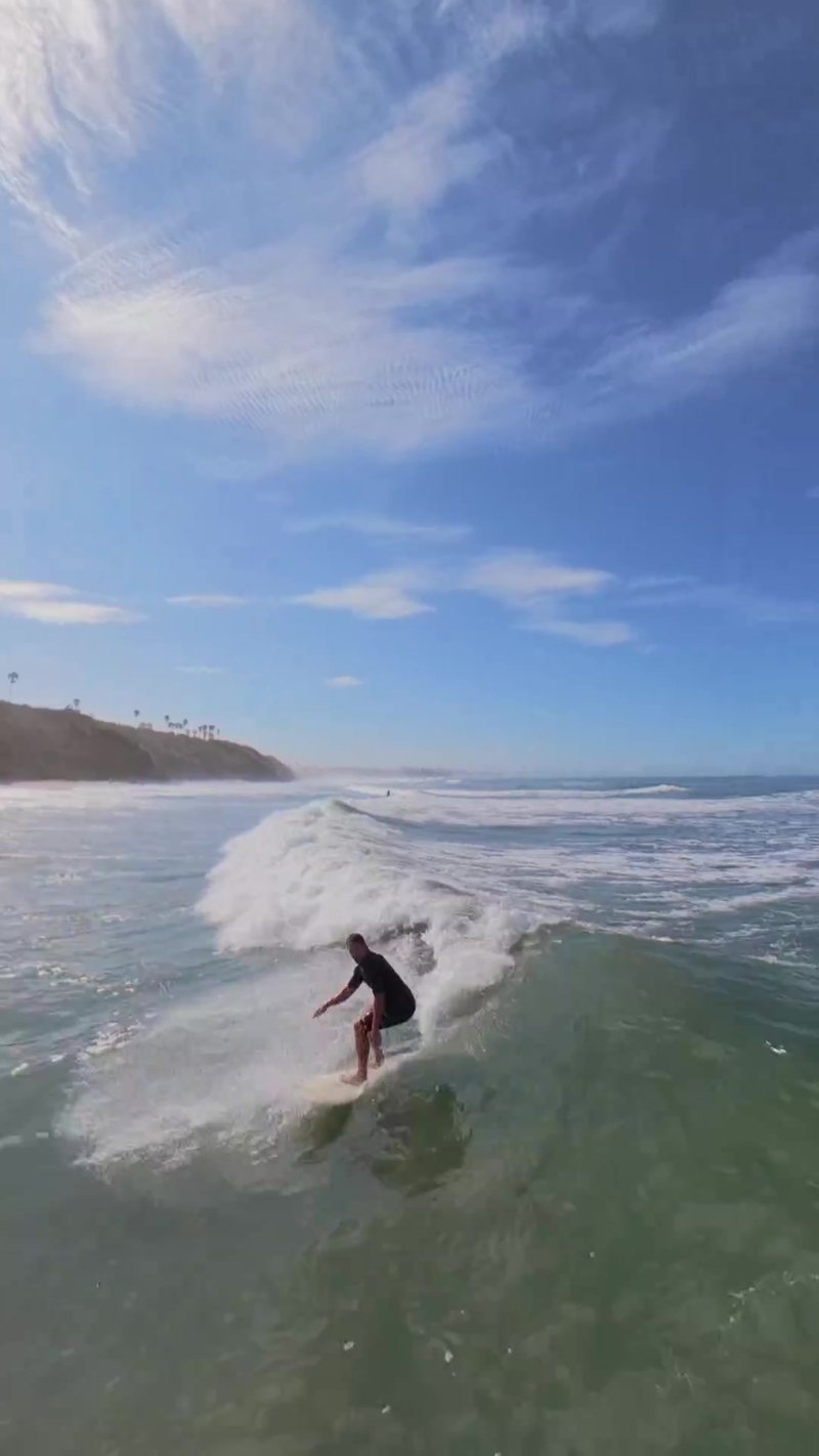FPV aerial follow low and close alongside a surfer riding down the line at Pipes, Encinitas